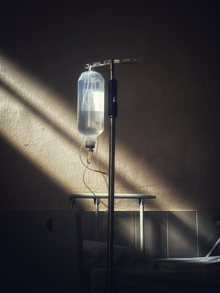 services-04 An intravenous drip stand in a quiet hospital room with soft lighting, representing healthcare and solitude.